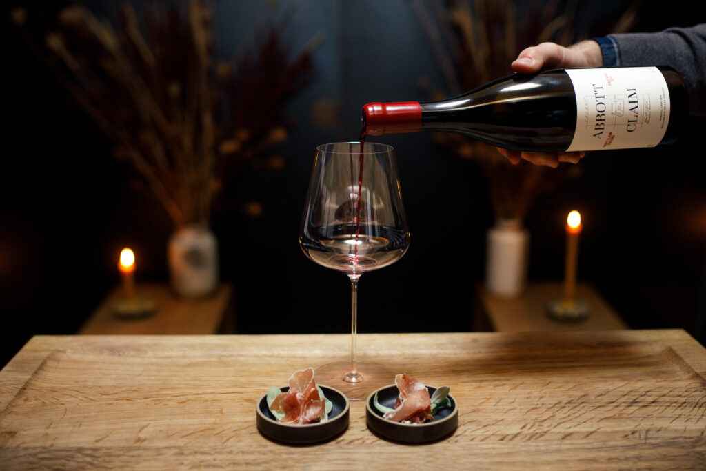 pouring wine into a glass with two small plates of charcuterie.