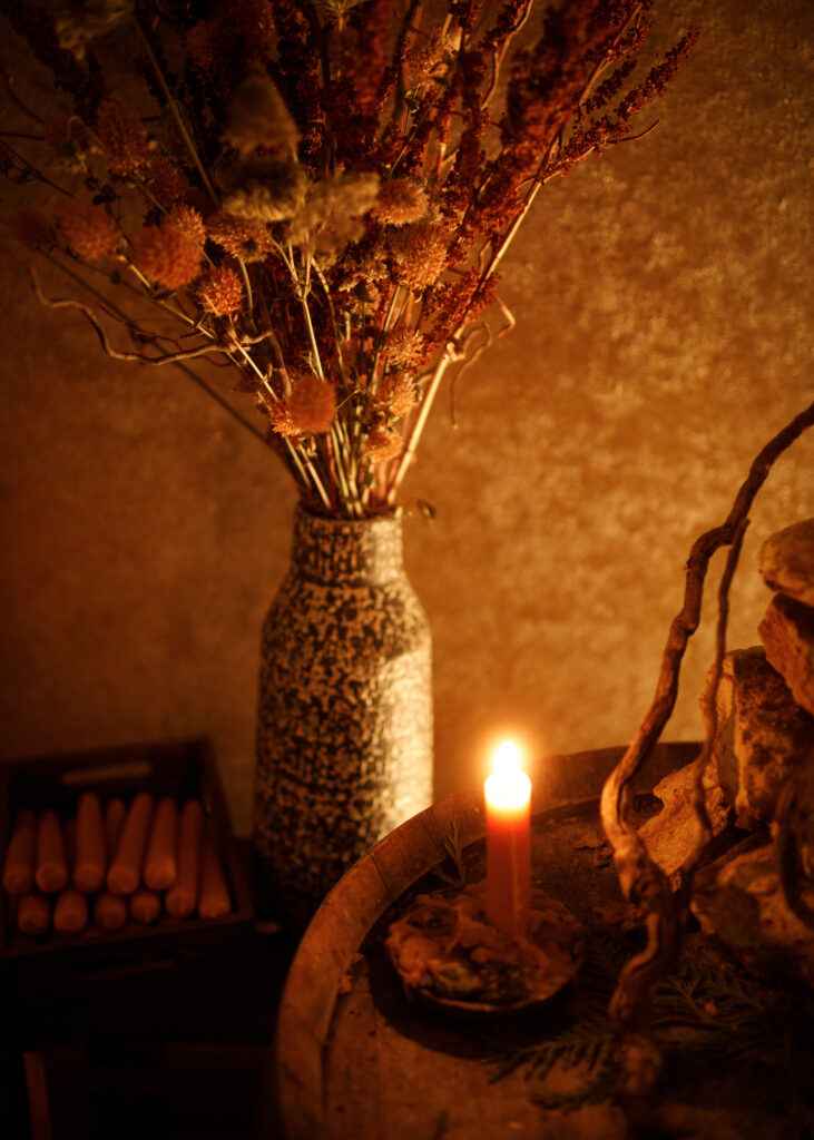 A candle is lit on a table next to a vase of flowers.