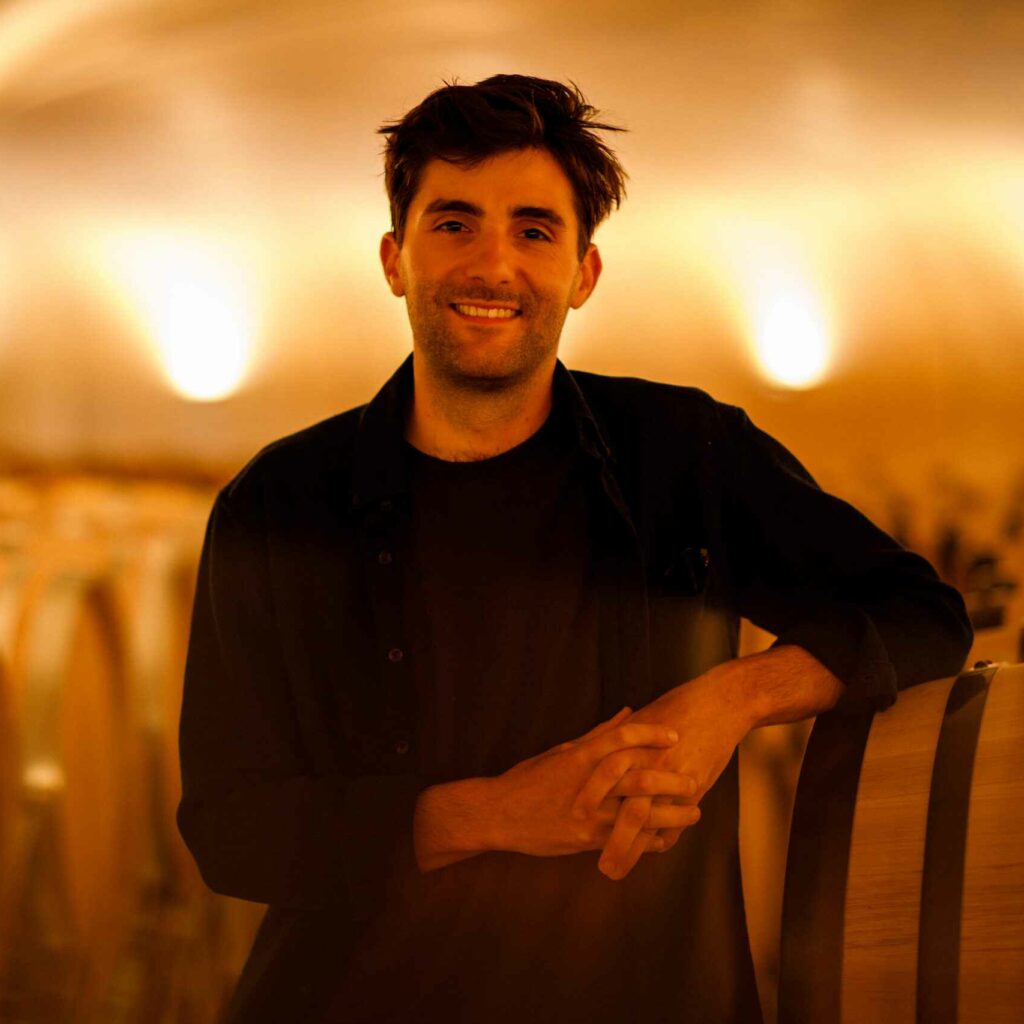 Alban smiling in front of wine barrels.