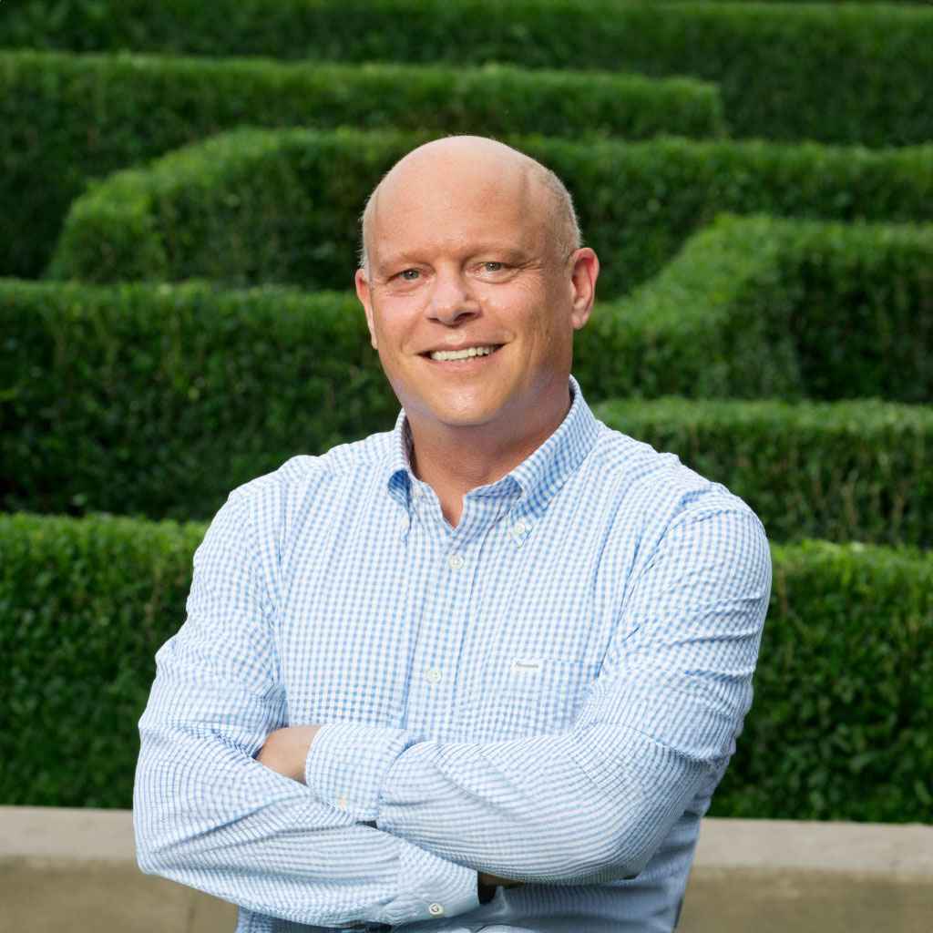 A bald man standing in front of a hedge maze.